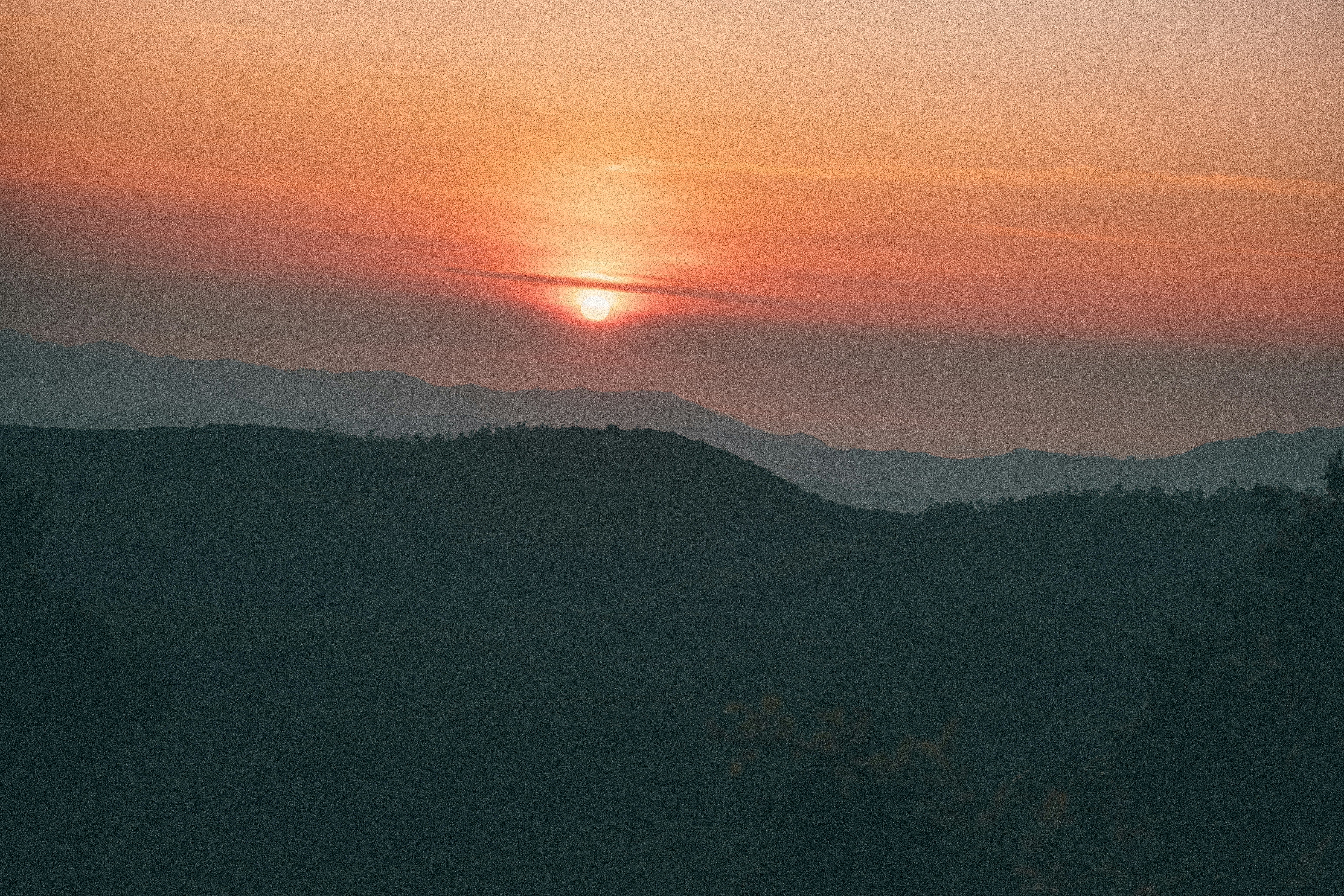 A warm, hazy sunset dipping behind layered mountain silhouettes